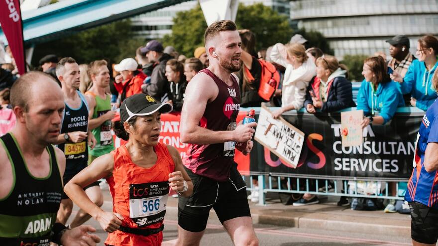 A man running in a Mencap running vest in front of cheering crowds who are lining the street on part of the course