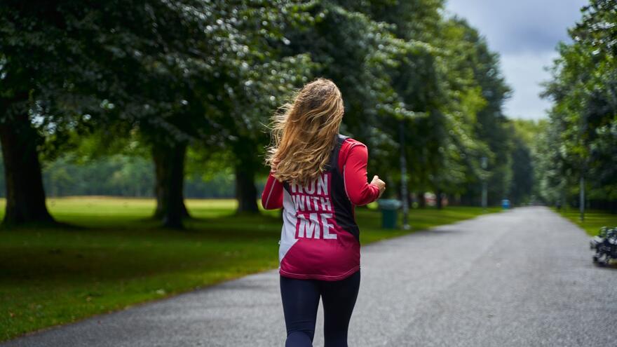The back of a woman with long hair running along a path in a park with a Mencap T-shirt on