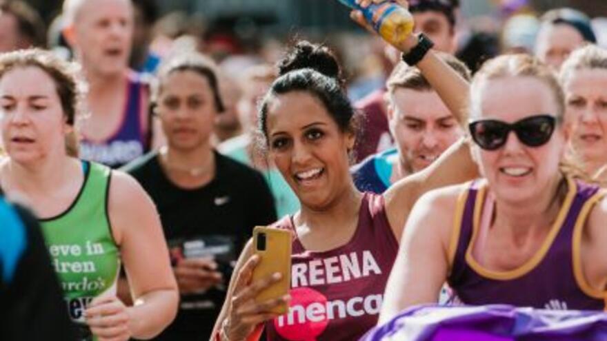 A woman running a marathon in a Mencap running vest smiling to the camera and waving a water bottle
