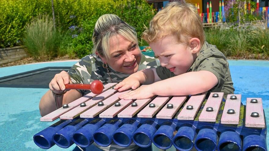 A mother playing a xylophone with her son in a sensory outdoor play area.