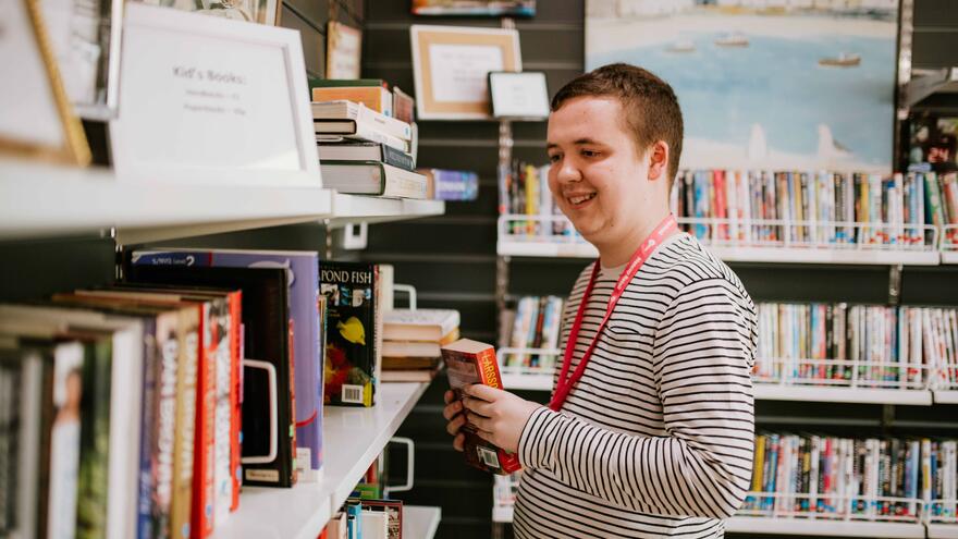 A man taking a book off a bookshelf in the Clacton Mencap shop