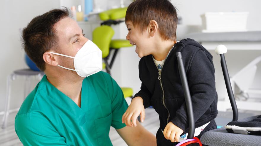 A nurse wearing a mask laughing with a child in a treatment room