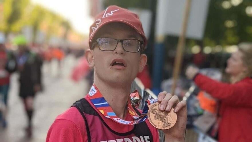 Freddie in a Mencap running vest showing his marathon medal to the camera and crowds