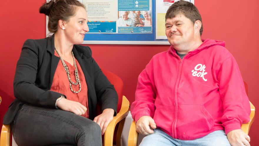 A woman and man are talking to each other as they sit in a waiting room