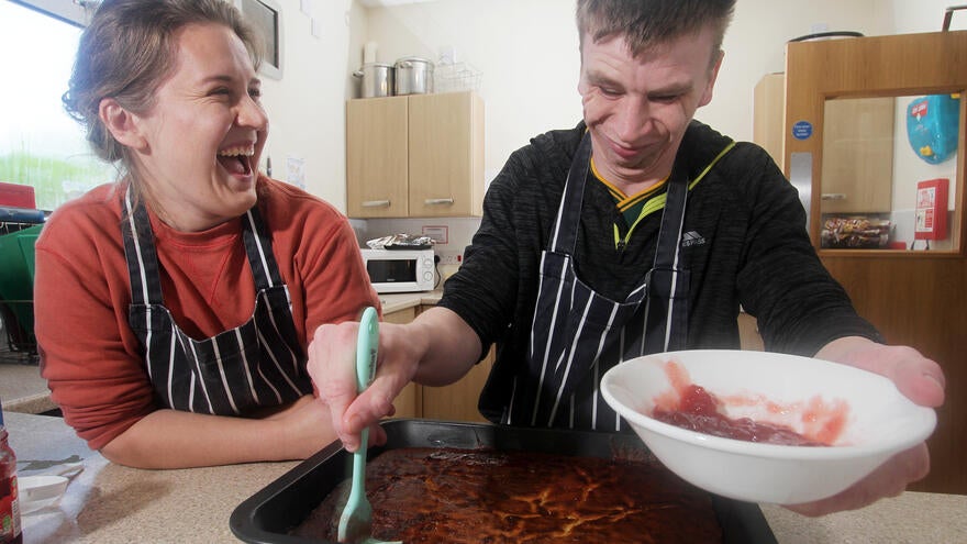 A woman and a man laughing while making a cake. 