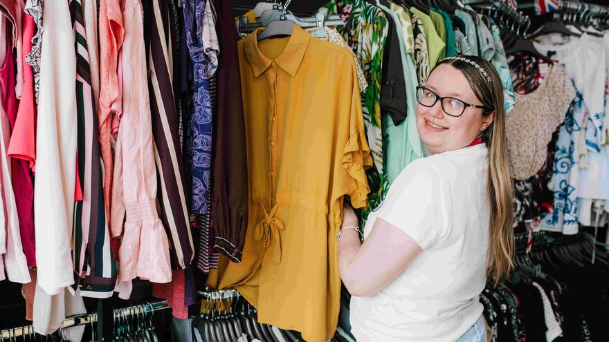 A sales assistant in a Mencap shop going through a rail of women's tops 