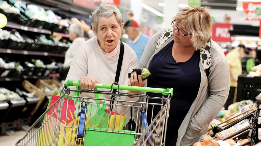 A support worker is helping an older woman to shop for groceries in a supermarket