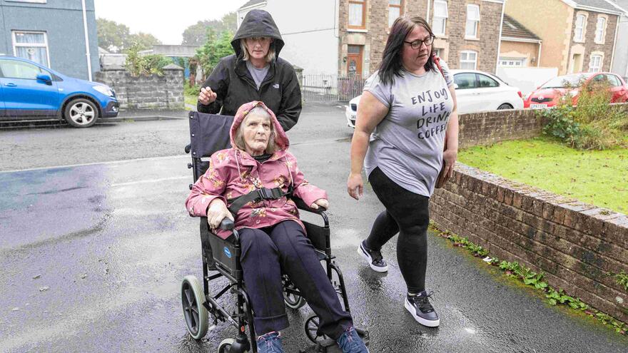 Two support workers taking a woman in a wheelchair for a walk outside