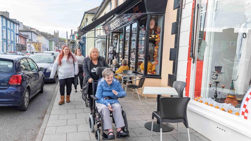 Carer pushing a woman in a wheelchair through a high street