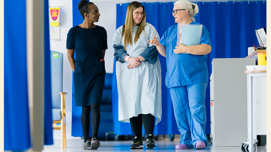 Two healthcare professionals are walking a patient down a ward in a hospital