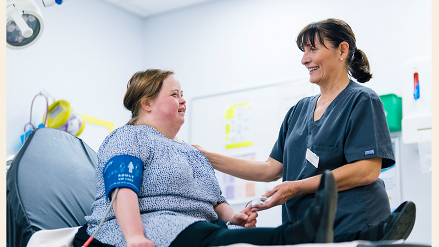 A doctor reassures a patient with Downs Syndrome who is lying on a bed