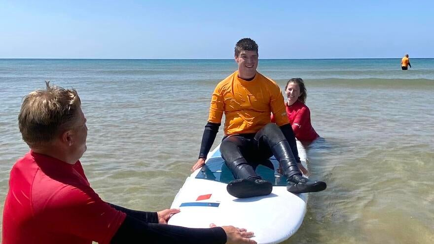 A man sitting on a surfboard that is being held in the water by two surf instructors