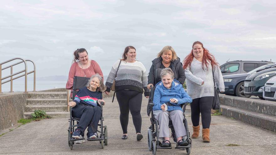 A group of support workers taking two women in wheelchairs out for the day along the sea front