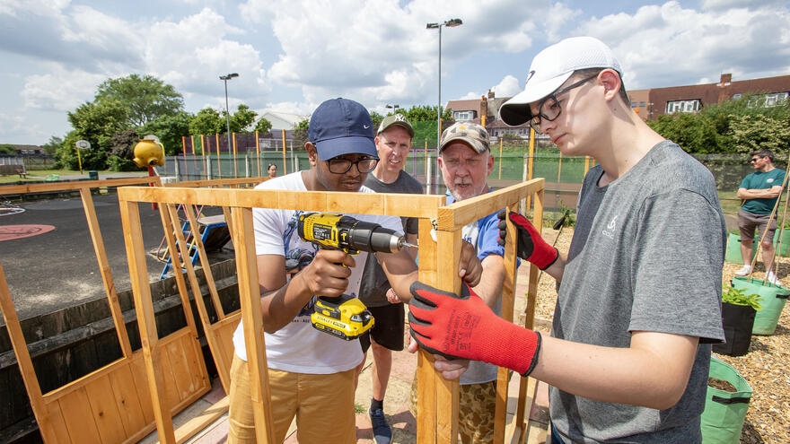 A man drilling a wooden frame with some helpers