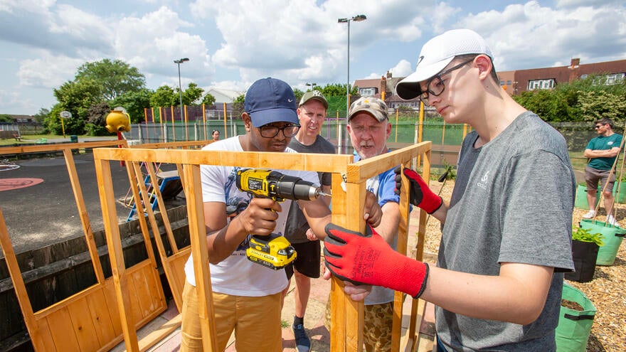 A man drilling a wooden frame with some helpers