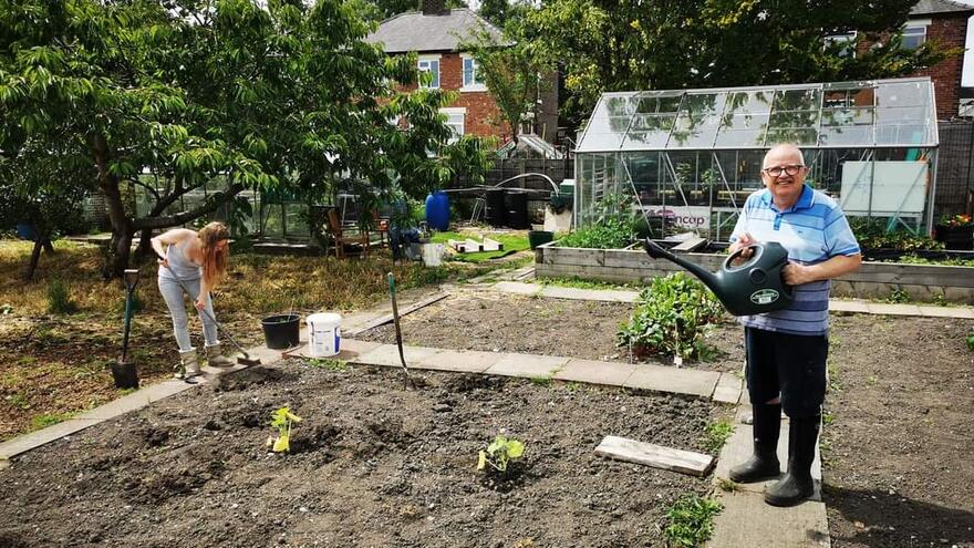 A man standing in an allotment with a watering can.