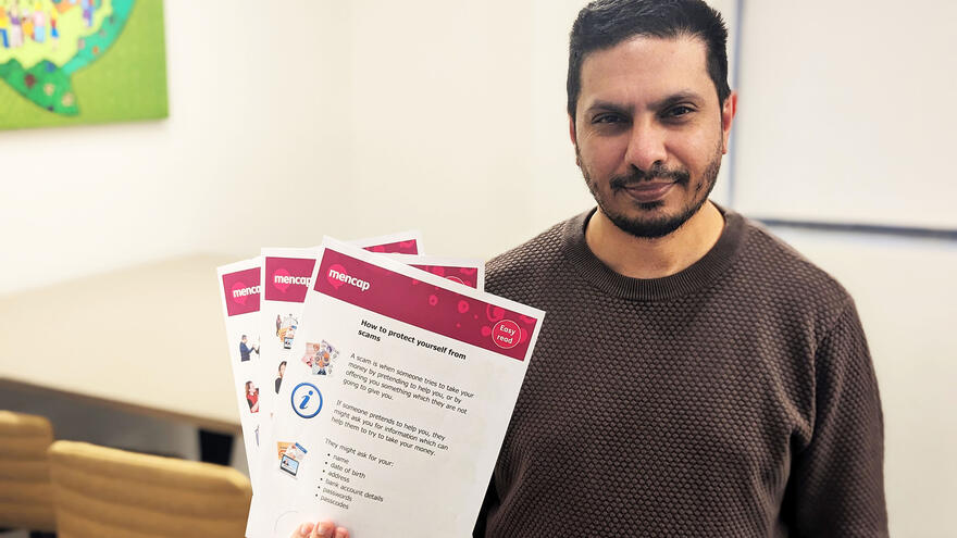 A man with short dark hair and a beard holding sheets of paper fanned out in front of him