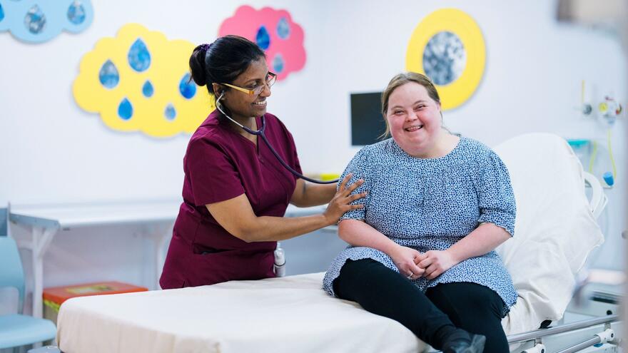 A woman with Down syndrome sitting on a hospital bed being examined by a doctor