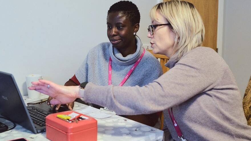 A support worker helps someone on a laptop sitting at a desk