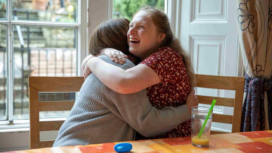 A young girl hugs her support worker while they are sat at a table