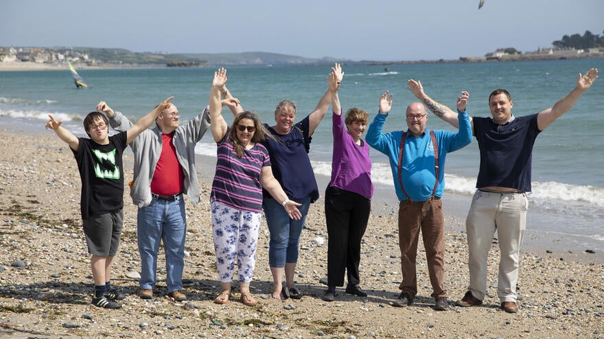 A group of people standing on a beach all happily raising their hands up in the air.
