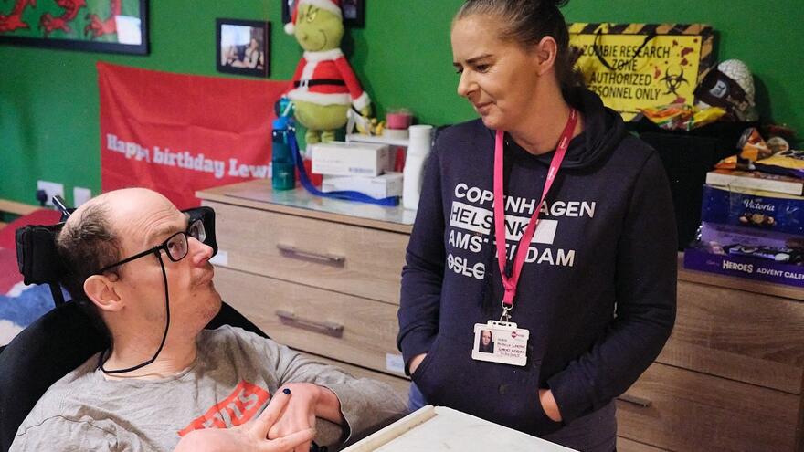 A support worker crouches down next to a man in a wheelchair