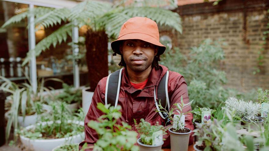 Mel is in a greenhouse surrounded by plants