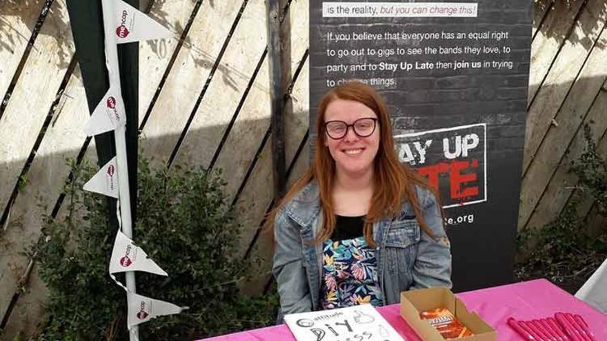 A young woman sits outside at a decorated table selling merchandise and giving out free leaflets about Mencap and the importance of fundraising
