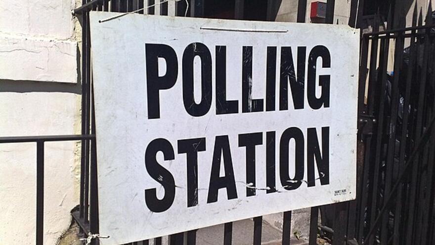 A white sign with black letters reading "Polling Station" attached to a fence.