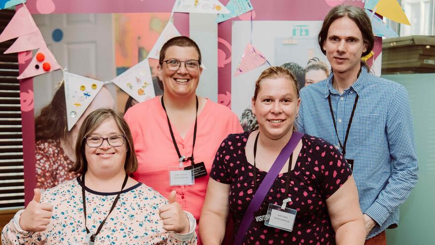 Four Mencap representatives standing in front of two Mencap banners
