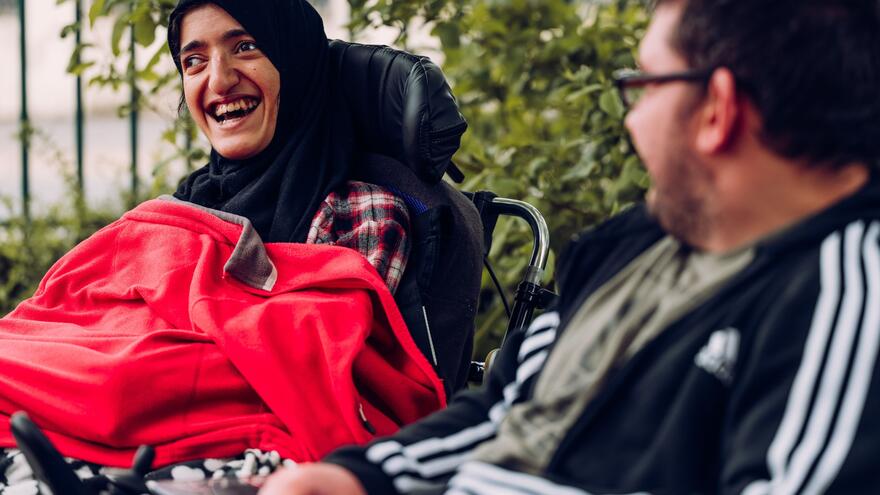 A woman and a man who are both in wheelchairs in a park are talking and laughing