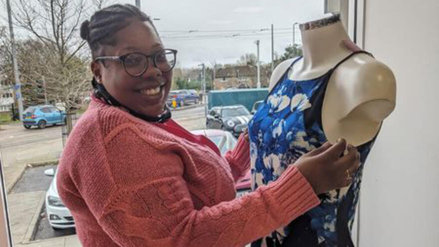 A woman smiles as she fits a dress onto a shop mannequin