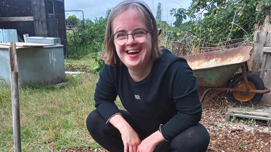 A woman with glasses smiling, kneeling down on an allotment growing bed