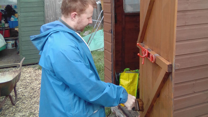 A man in a blue coat paints a shed door