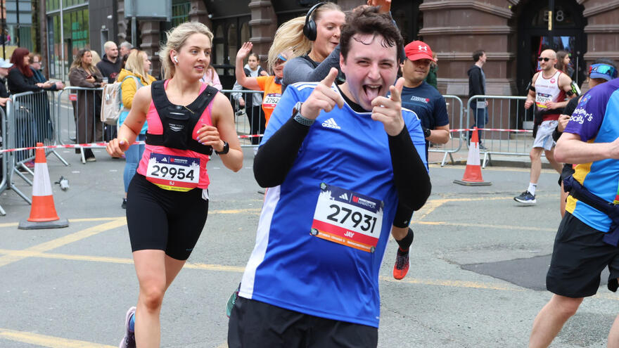 A man pointing to the camera as he runs alongside other runners on a city street