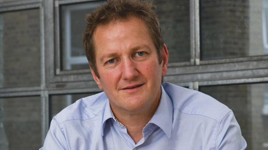 A man in a blue shirt with short dark hair looking at the camera