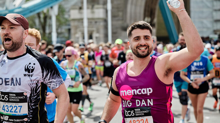 Man running in a Mencap vest on a road one arm in air