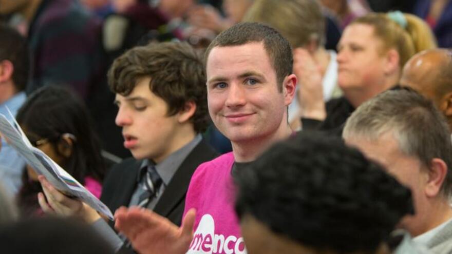 A man in a crowd smiling at the camera wearing a Mencap Tshirt