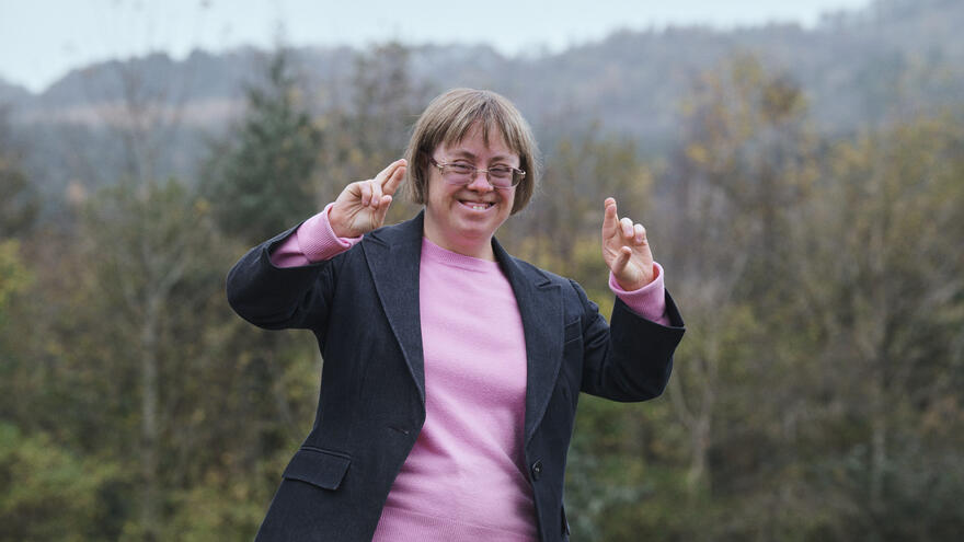 Sara Pickard with her fingers crossed, standing outside with trees behind her