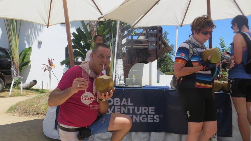 Richard under the shade of an umbrella drinking from a coconut