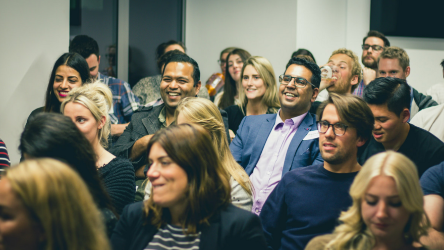 A group of smiling attendees listening to someone talking