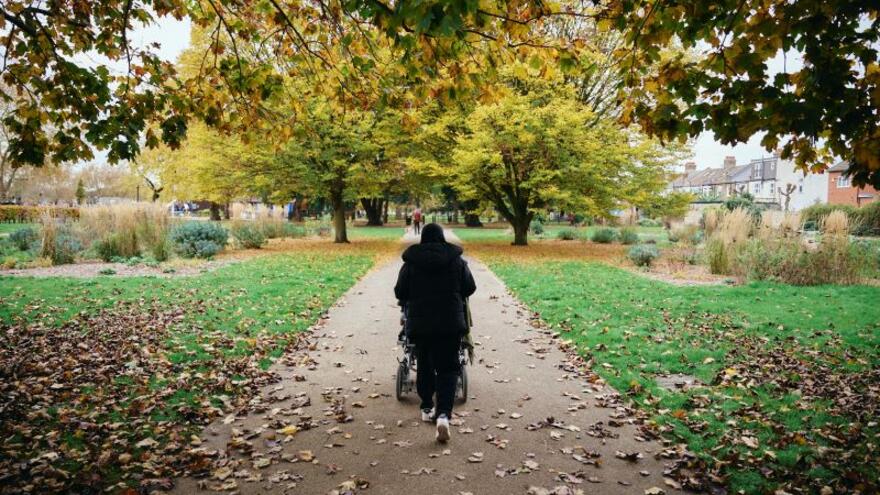Rahima in a park being wheeled away down a path by her carer