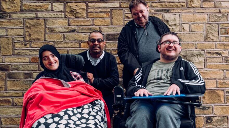 A group photograph showing two people with learning disabilities in wheelchairs with their carers
