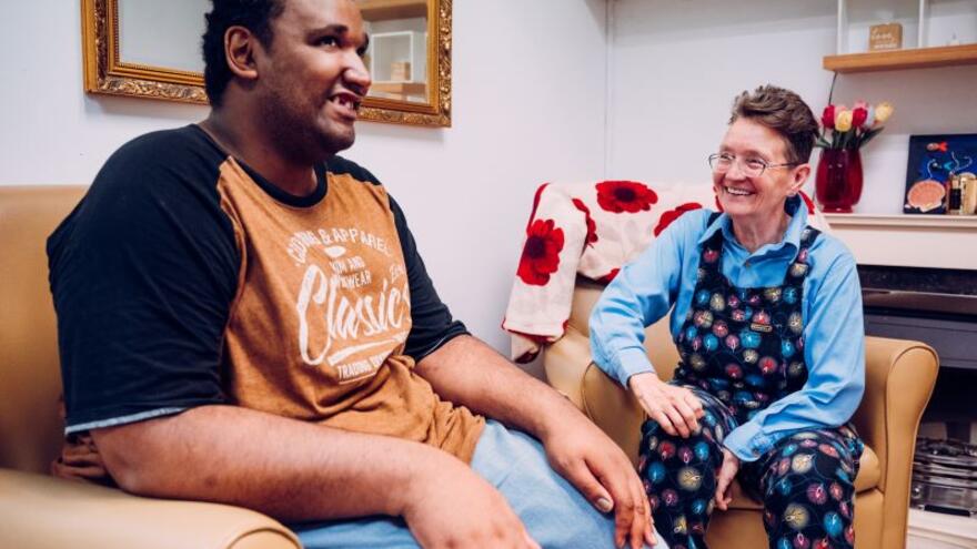 A man sitting in a living room on a chair next to a woman who is also on a chair