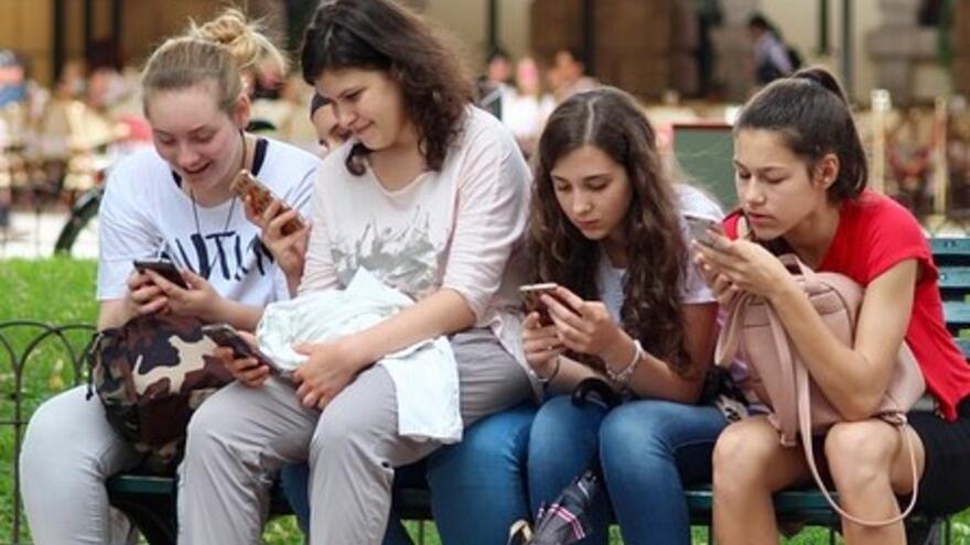 Four young women on a park bench looking at their mobile phones