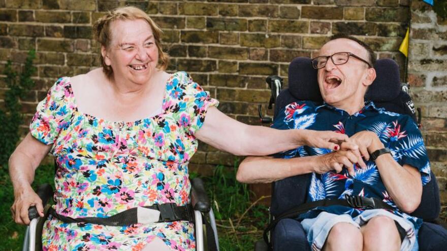 Barry and Betty sitting together outside smiling and holding hands