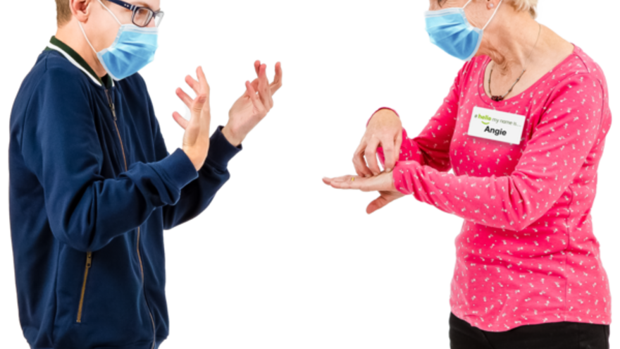 A woman using sign language to a young man. Both are wearing face masks