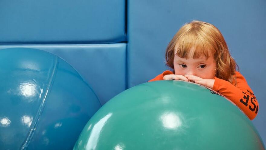 Young child in a soft play room hiding behind a big bouncy ball