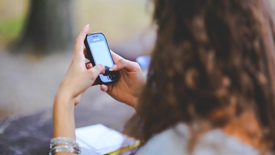 The back of a woman with long hair who is sitting down outside using a mobile phone