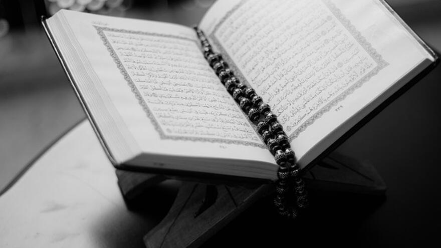 A photograph of the Quran open on a page with a string of beads